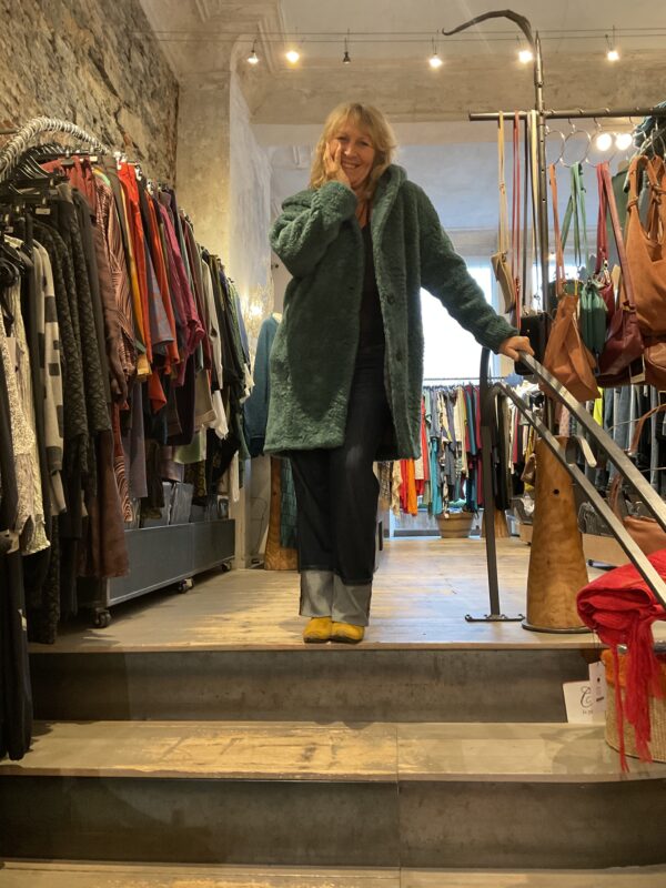 Grote maten mode Gent dames kledij en accessoires vrouwen. Middellange mantel met grote kap in blauw groene stof met wol en zelfde kleur voering van Fox’s