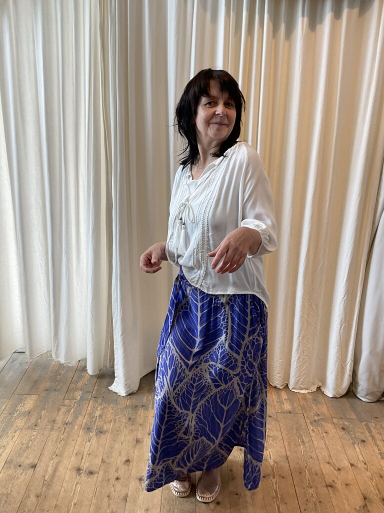 Kleurrijke, creatieve en unieke mode voor dames in hartje Gent. Grote maten mode dames kledij en accessoires voor vrouwen met een maatje meer of minder. Rok in soepele en lichte stof en koningsblauw paarse print met grijs van Bindi. Losse blouse in ecrumet halflange mouwen van Bindi.